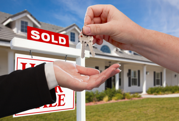 Handing Over the House Keys in Front of Sold New Home Against a Blue Sky